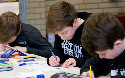 Drei Jungs arbeiten konzentriert an ihren Aufgaben an einem Tisch.