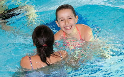 Zwei Schülerinnen schwimmen im Pool und haben Spaß im Wasser.
