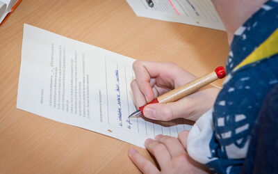 SchülerIn schreibt mit einem Füller auf ein Blatt Papier.