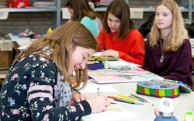 Eine Gruppe von Mädchen, die an ihren Kunstprojekten arbeitet, umgeben von Farben und Materialien.