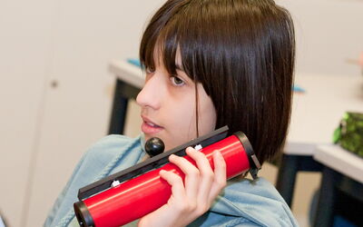 Schülerin hält roten Gegenstand wie ein Telefon an ihr Ohr.