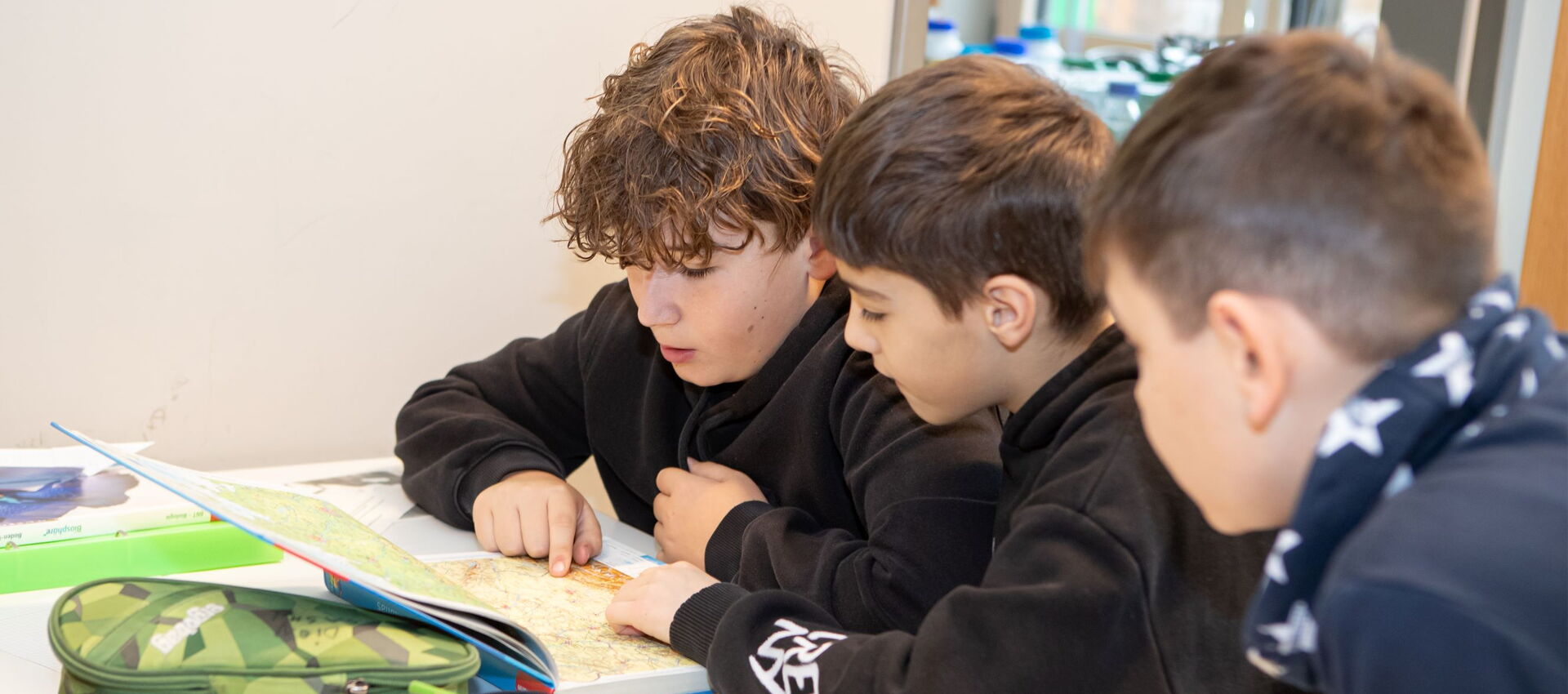 Drei Jungen lesen gemeinsam ein Buch über Naturwissenschaften und lernen dabei miteinander.