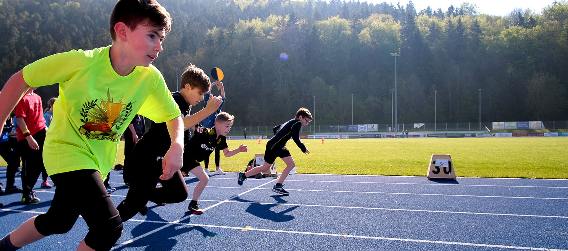 Auf einer Laufbahn rennen junge Kinder während sie Sportunterricht haben.