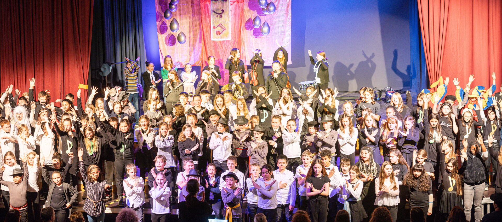 Auf der Bühne stehen viele Schüler mit erhobenen Händen beim Unterstufenball "Der magische Kontrabass"