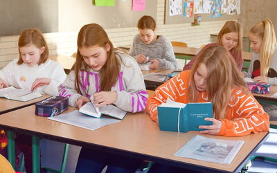 Schülerinnen sitzen an ihren Tischen in einem Klassenzimmer und arbeiten an ihren Aufgaben.