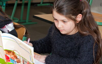 Ein junges Mädchen liest ein Buch in einem Klassenzimmer.
