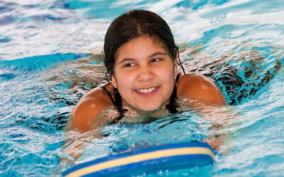 Ein lächelndes Mädchen schwimmt mit Schwimmbrett im Pool.
