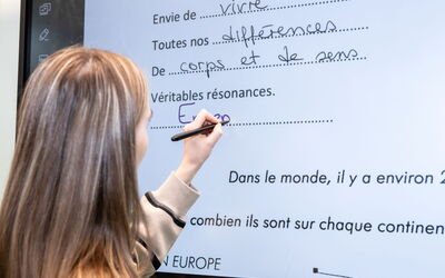 Eine Schülerin schreibt mit einem Stift auf ein Whiteboard.