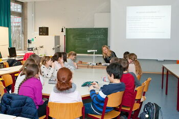 Eine Gruppe von SchülerInnen sitzt mit einer Lehrerin um einen Tisch in einem Klassenzimmer und diskutiert gemeinsam.