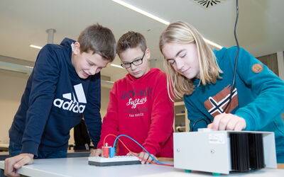 Drei Schüler arbeiten in einem Labor an einem technischen Gerät für den Physikunterricht.