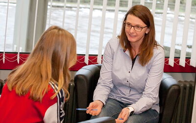 Eine Frau sitzt in einem Stuhl und spricht mit einem Mädchen, das ihr gegenüber sitzt.