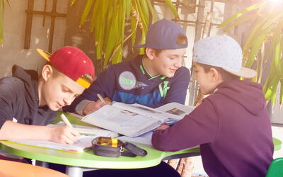 Drei Schüler sitzen an einem Tisch und arbeiten gemeinsam im Gang.