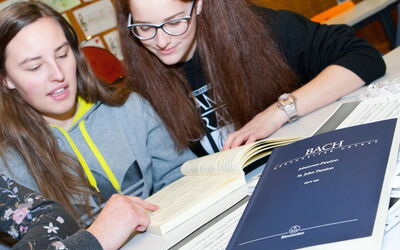 Schülerinnen betrachten ein Musikbuch in einem Klassenzimmer und tauschen sich darüber aus.