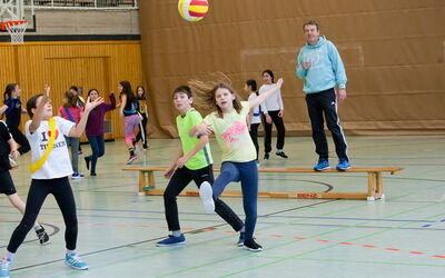 Eine Gruppe von SchülerInnen spielt Volleyball in einer Sporthalle. Sie lachen und haben viel Spaß beim Spielen.
