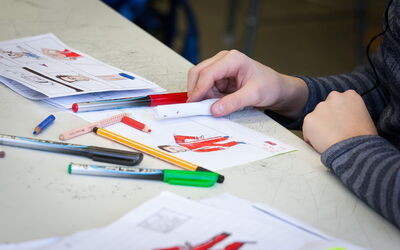 SchülerIn malt mit einem Stift auf einem Blatt Papier und zeigt künstlerische Fähigkeiten.