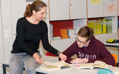 Eine Lehrerin erklärt einem Schüler in einem Klassenzimmer etwas aus einem Buch, um ihm zu helfen.