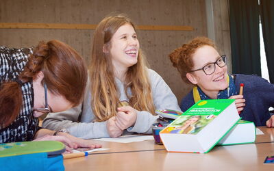 Drei Schülerinnen sitzen an einem Tisch und unterhalten sich fröhlich miteinander.