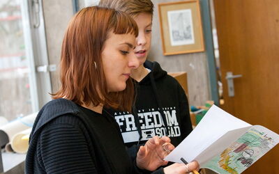 Schüler und Lehrerin schauen gemeinsam in ein Buch und diskutieren darüber.