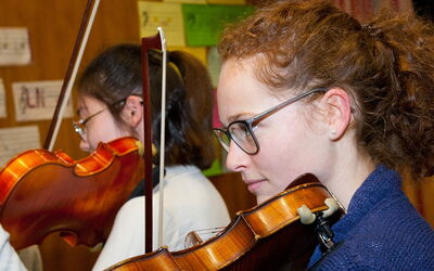 Zwei Schülerinnen spielen in einem Klassenzimmer Geige und teilen ihre Leidenschaft für die Musik.