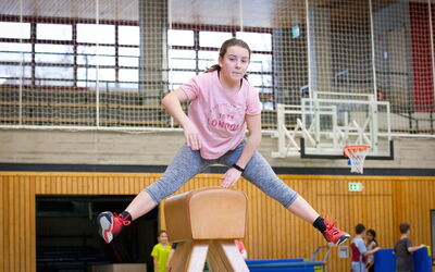 Ein Mädchen springt über einen Holzbock in einer Turnhalle.