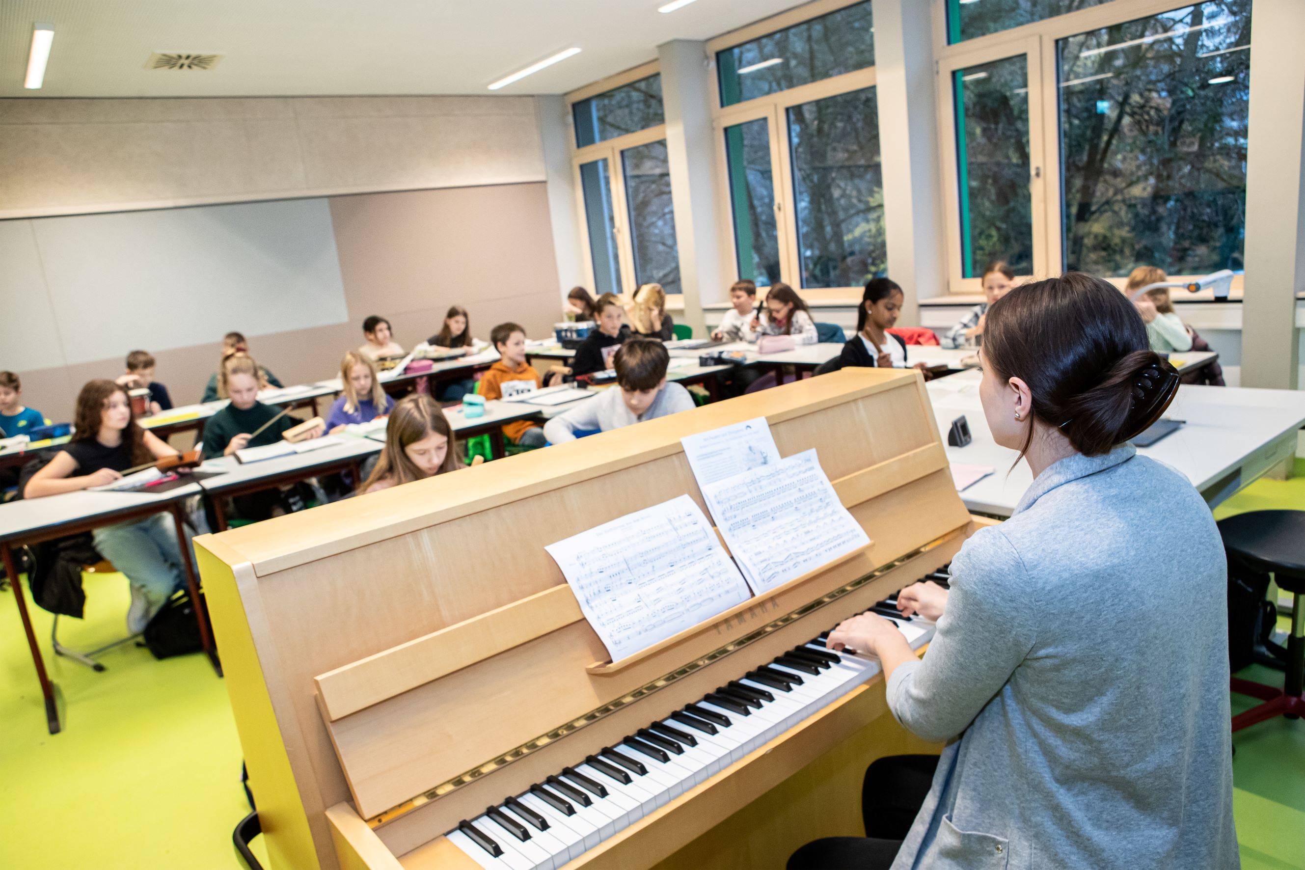 Lehrerin spielt Klavier im Klassenzimmer voller SchülerInnen.