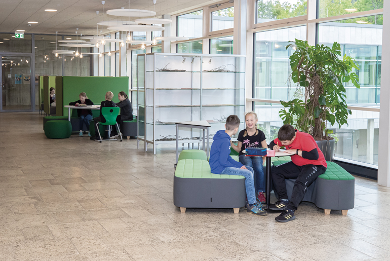 SchülerInnen sitzen in Gruppen an Tische und machen ihre Aufgaben.