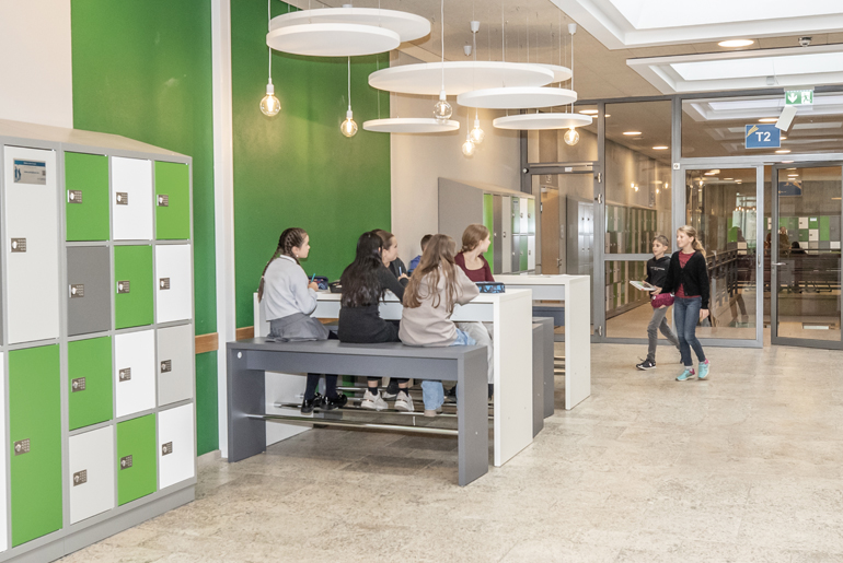 SchülerInnen sitzen an Tischen neben einem Spind.